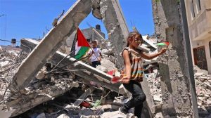 Anak-anak Palestina mengibarkan bendera nasional Palestina saat mereka bermain di antara puing-puing bangunan yang dihancurkan oleh pemboman Israel di Gaza selatan, 19 Juni 2021