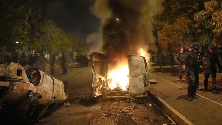 Pasukan polisi berjalan melewati mobil yang terbakar di Nanterre, di luar Paris, 29 Juni 2023.